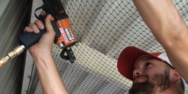Man using a power tool on a wire fence.