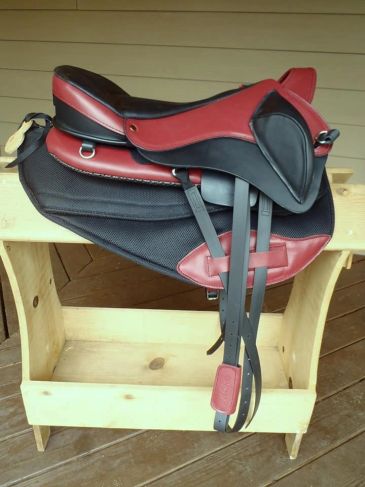 Red and black horse saddle on wooden stand.