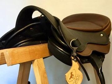 A black and brown horse saddle with a tag, resting on a wooden stand.