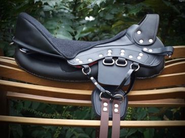 Black leather horse saddle on wooden rail.