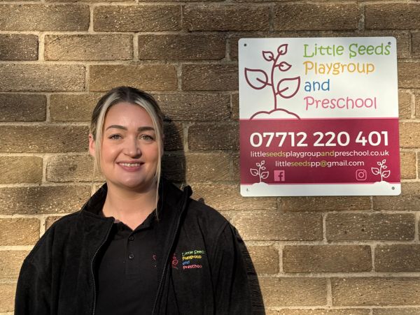 Woman standing next to a Little Seeds Playgroup and Preschool sign.