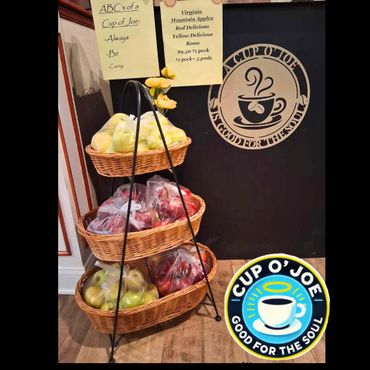 Three-tier basket stand with bags of apples and a 'Cup O' Joe' sign.