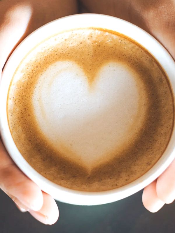 Hands holding a cup of coffee with a heart-shaped foam design.