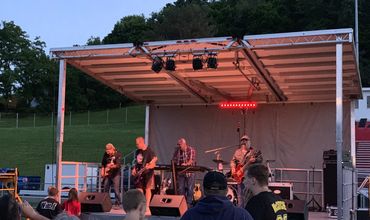 Rock band performing on a mobile stage with overhead truss lighting at an evening festival