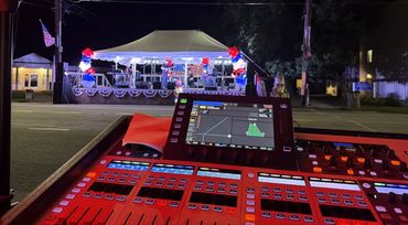 Mixing console at front of house for a band on a lit outdoor festival stage at night