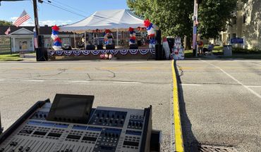 Festival stage with PA speakers, tent and cable ramp, seen from the sound booth