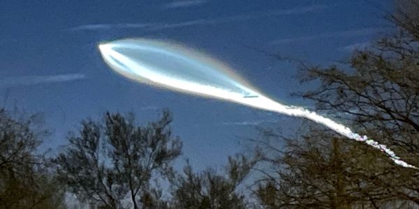 Blue Origin space rocket going through sky above forest of trees