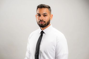 Professional portrait of a man in a white shirt and black tie against a plain background.