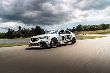 A white Honda Racing car speeds on a racetrack under cloudy skies.