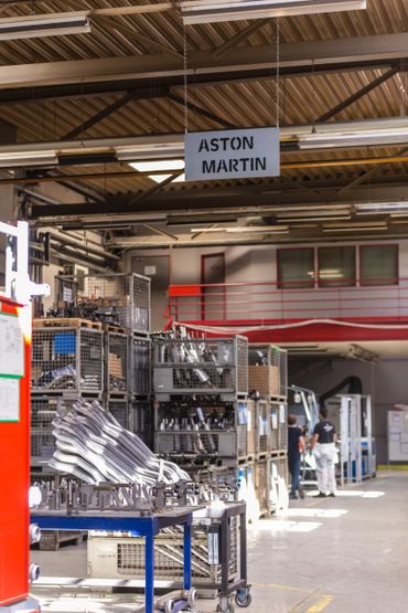 A factory section labeled Aston Martin with metal parts and workers.