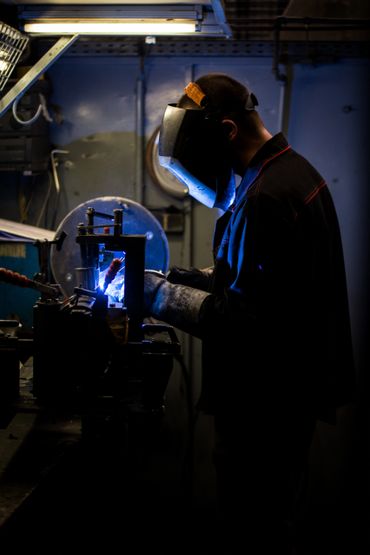 Welder working with protective gear in a dimly lit workshop.