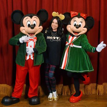 A woman poses with Mickey and Minnie Mouse in festive outfits.