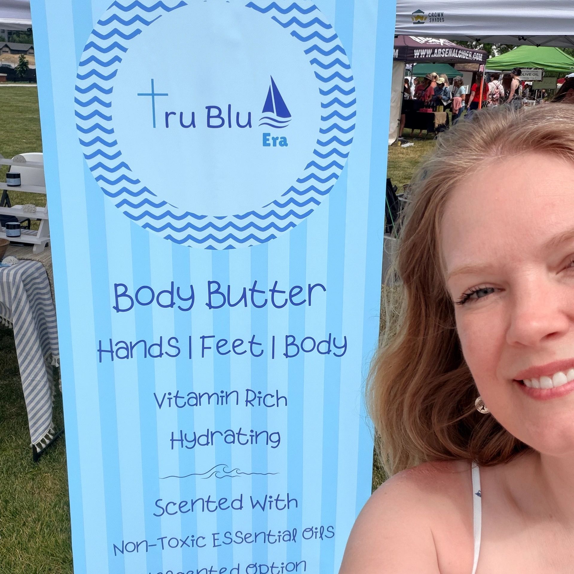 Blue Tru Blu Era body butter sign with smiling woman at outdoor market.