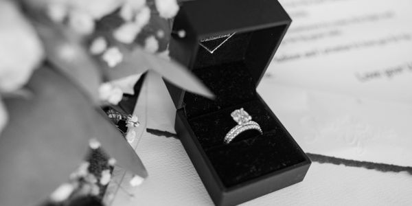 Engagement ring in a black box with flowers and a letter in the background.