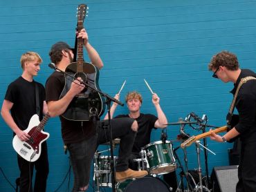 Band performing with instruments against a blue wall.