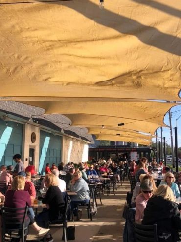 People dining outdoors under beige canvas canopies.