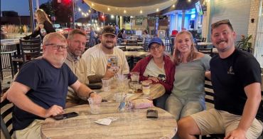 Group of six friends smiling at an outdoor restaurant.