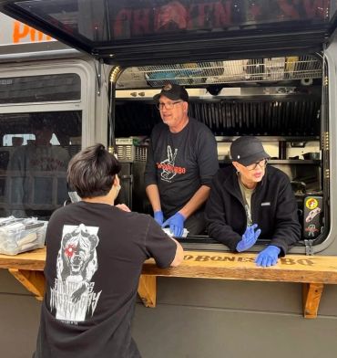 People interacting at a food truck serving BBQ.