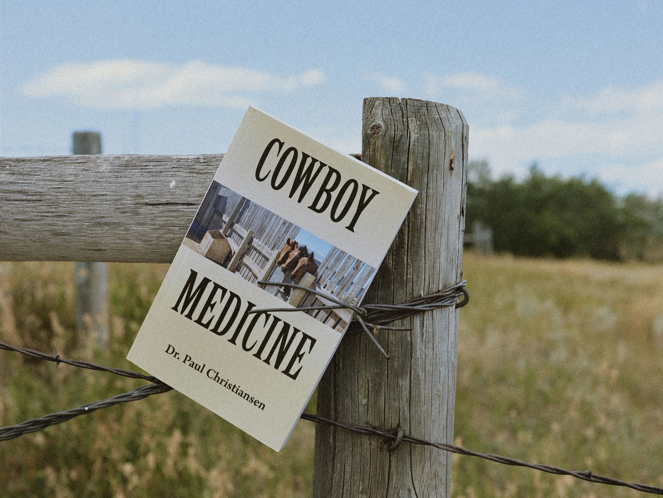 A flyer about cowboy medicine pinned to a wooden fence post with barbed wire.