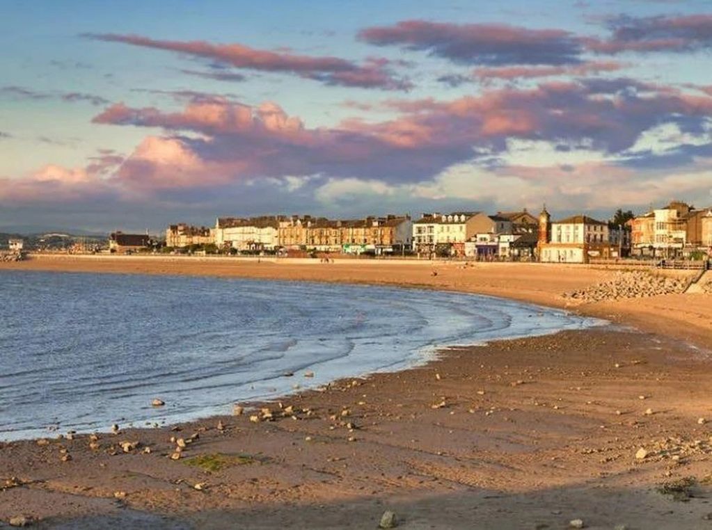 A calm beach with buildings along the shoreline under a colorful sky.
