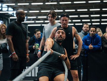 Man intensely pulling a rope in a gym competition with focused spectators.