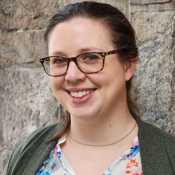 Smiling woman with glasses against a stone wall.