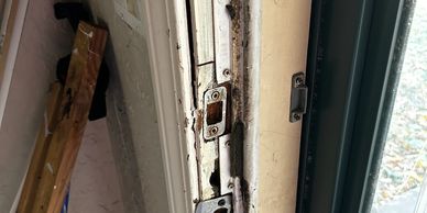 Close-up of a damaged door frame with chipped paint and exposed wood near a window.