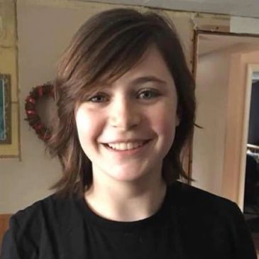 Smiling young person with short brown hair indoors.