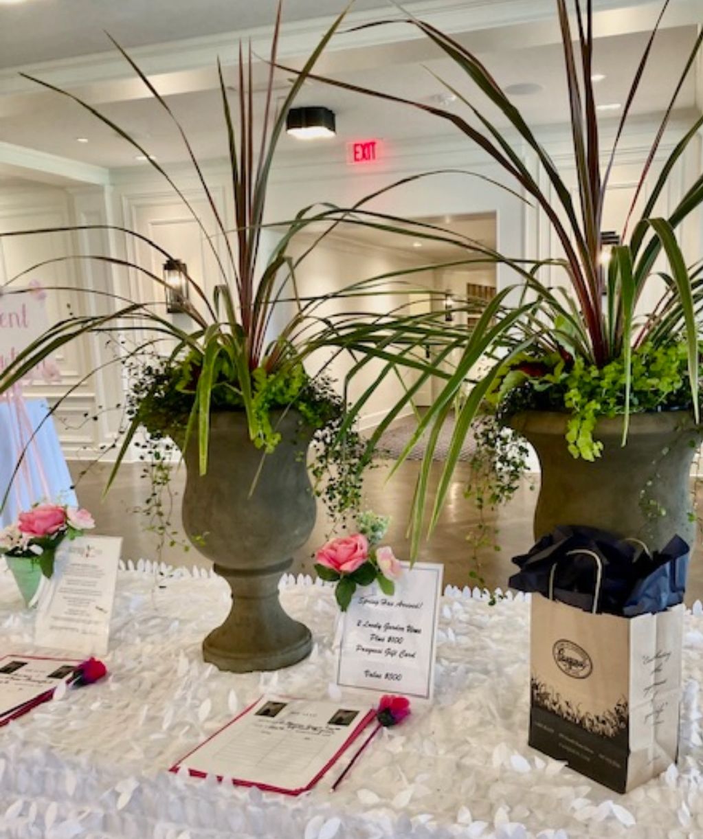Decorative plants and pink roses on a white tablecloth at an indoor event.