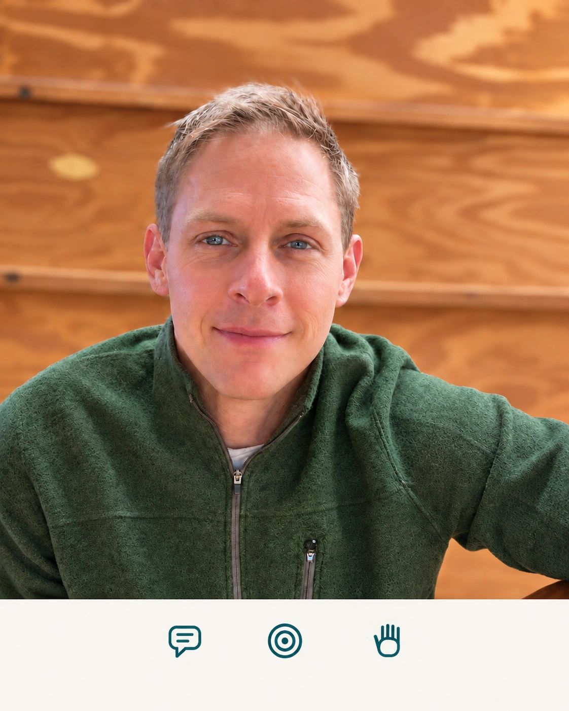 Smiling man in a green jacket against a wooden backdrop.