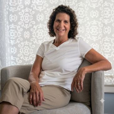 Woman smiling while sitting on a gray chair.