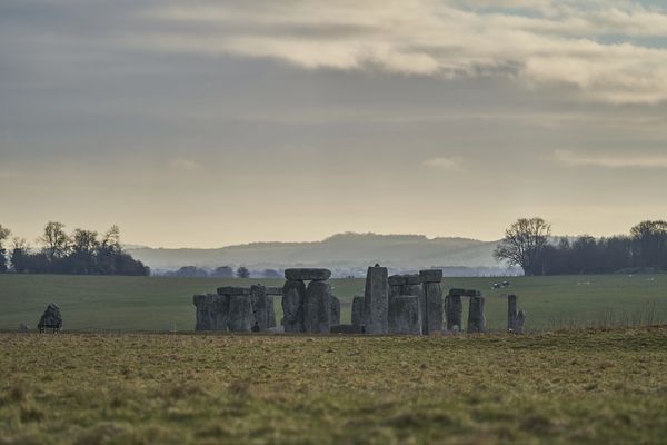 Stonehenge standing in a vast grassy field under a cloudy sky.