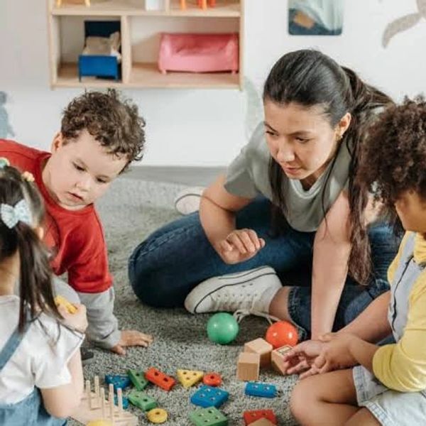 Teacher and children playing with blocks on the floor.