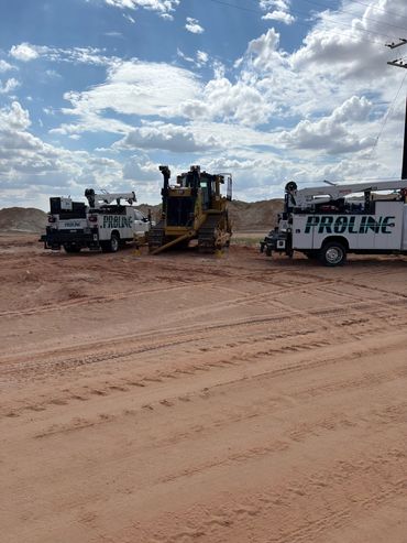 Heavy machinery and service trucks on a sandy construction site under a partly cloudy sky.