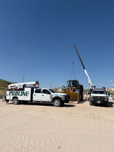 Two white service trucks with cranes lifting a large construction vehicle under a clear blue sky.