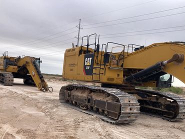 Two large yellow Caterpillar excavators on a dirt construction site under a cloudy sky.