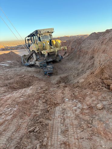 A bulldozer stuck in a dirt trench with a broken track.