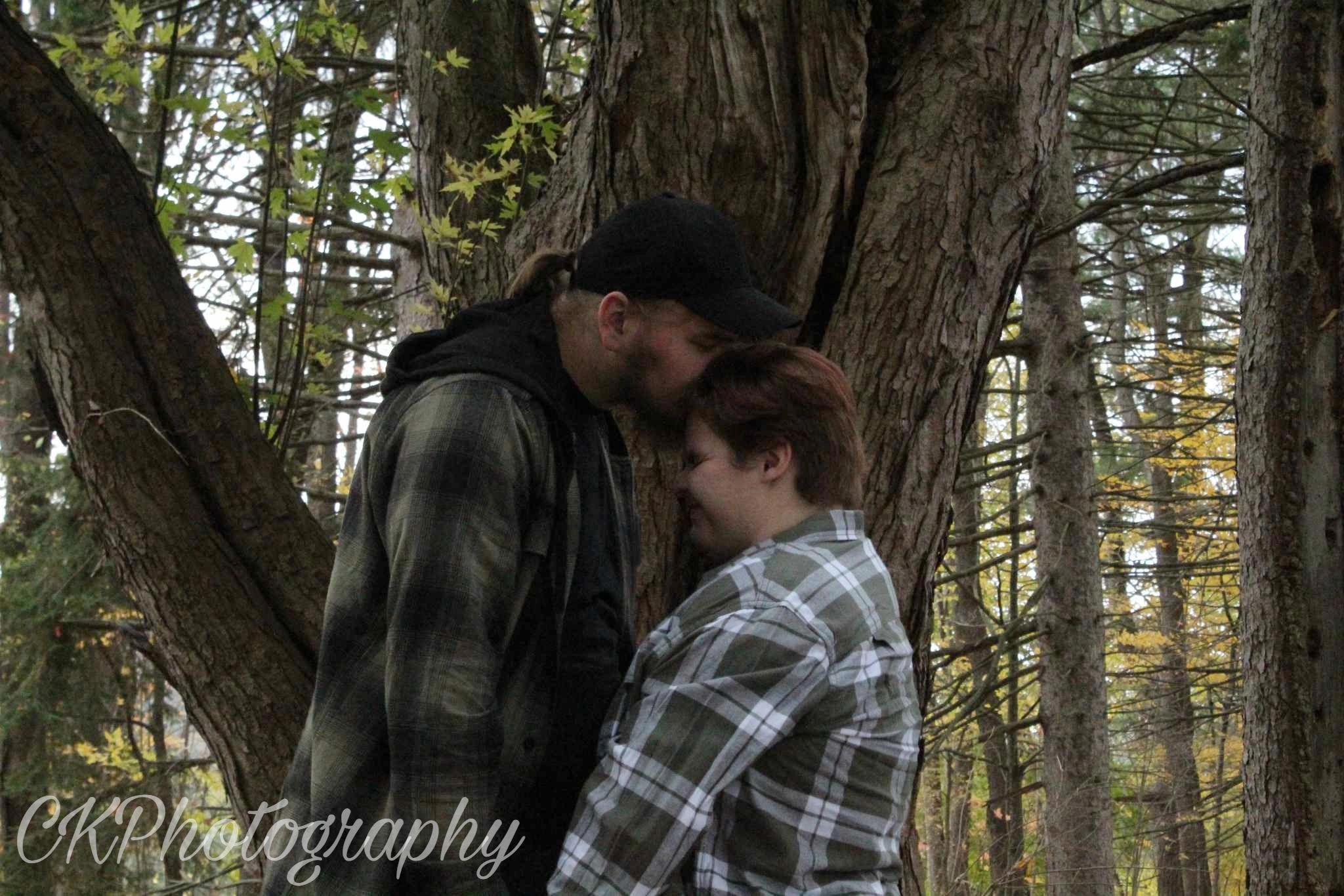 A couple sharing a tender moment in a forest, one kissing the other's forehead.