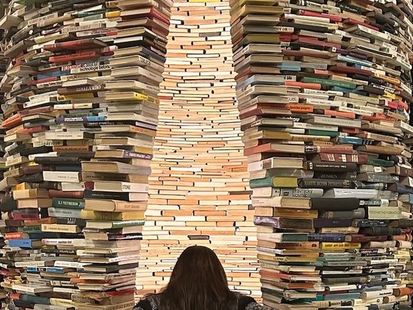 Person standing in front of a tall, circular stack of books with a narrow opening.