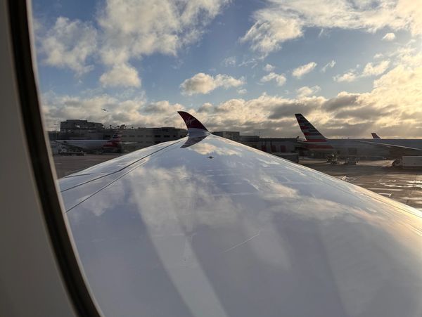 View of an airplane wing with sky and clouds reflected on it.