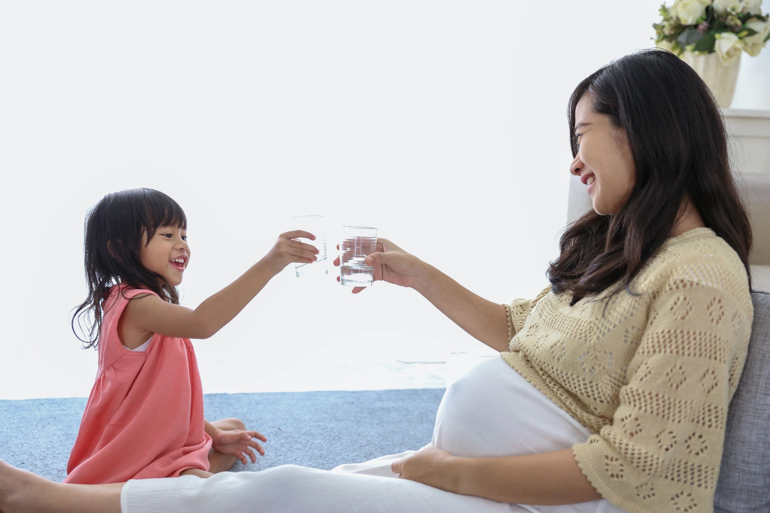 A pregnant woman and her child. Both are raising glasses and smiling at each other