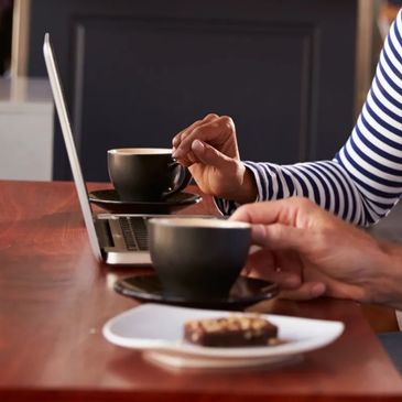 Couple having a coffee and slice on a wooden desk from matte black coffee cups, discussing finance