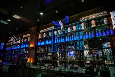 Bar shelf with mannequin heads and glowing blue bottles under dim lighting.