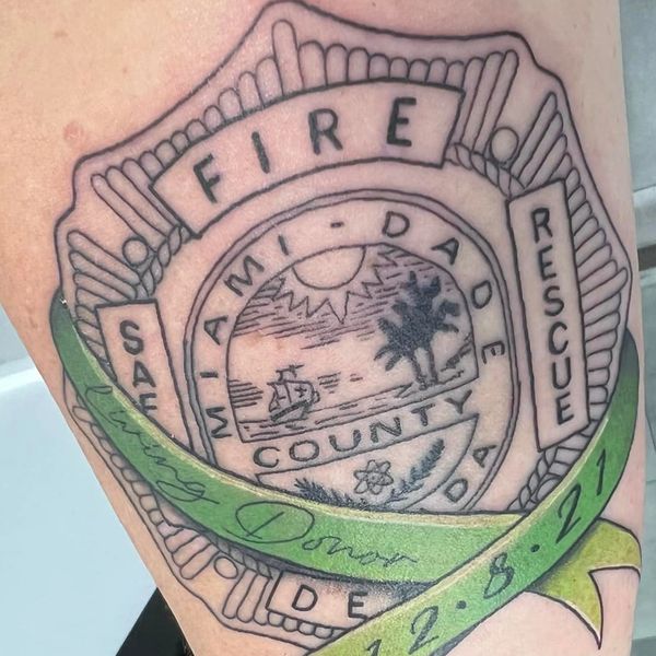 Tattoo of Miami-Dade Fire Rescue badge with a green ribbon and date.