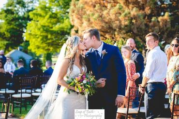 Bride and groom kissing at outdoor wedding ceremony.