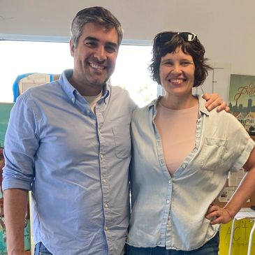 Two people smiling with arms around each other indoors.