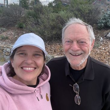A young woman and an elderly man smiling outdoors.