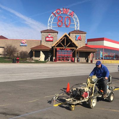 A man operates a line painting machine in front of a travel plaza with Wendy's and Dairy Queen signs.