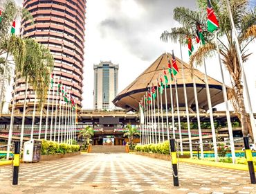 Kenyan Parliament buildings adorned with national flags under a cloudy sky.