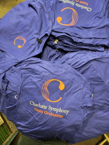 Purple Charlotte Symphony Youth Orchestras t-shirts with orange and white print.